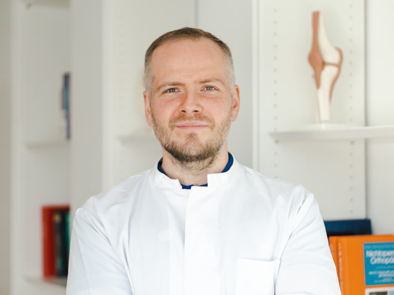 Dr. Wunderlich, der Münchner Orthopäde im weißen Arztkittel.